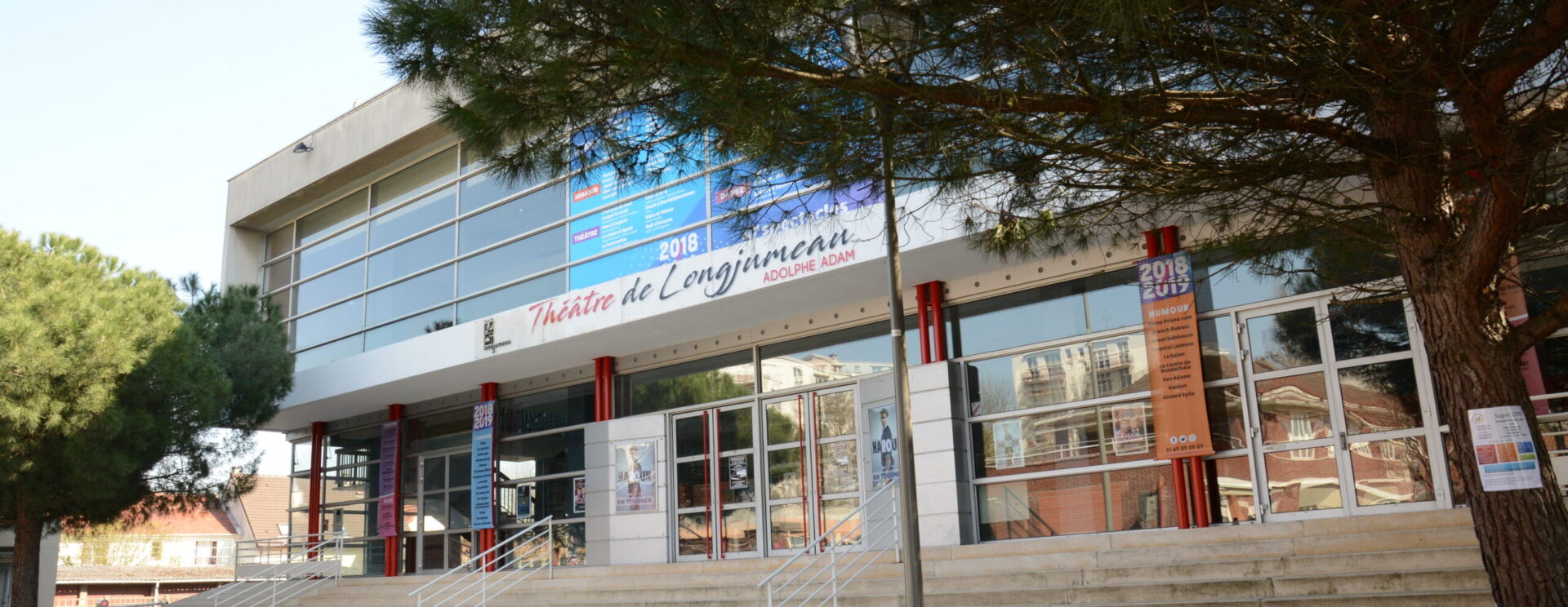 Une photo de l'entrée du Théâtre de Longjumeau avec plusieurs arbres et des marches devant l'entrée.